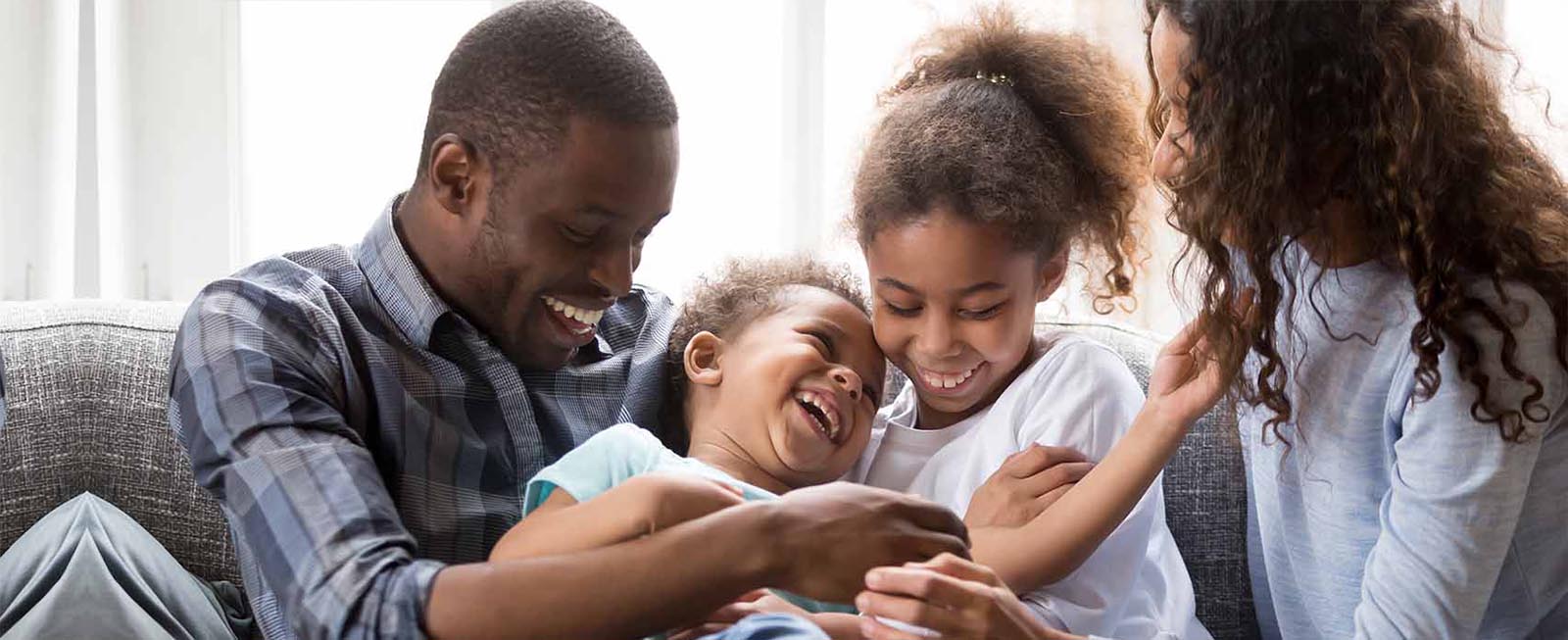 Happy black parents have fun with little mixed race kids tickling on couch at home, smiling African American family laugh playing together in living room, mom and dad relax on sofa with children